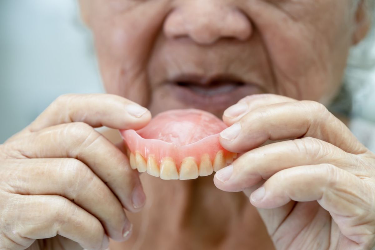 Senior holding dentures while considering advice from a dentist in Bentonville, AR about sleeping with dentures